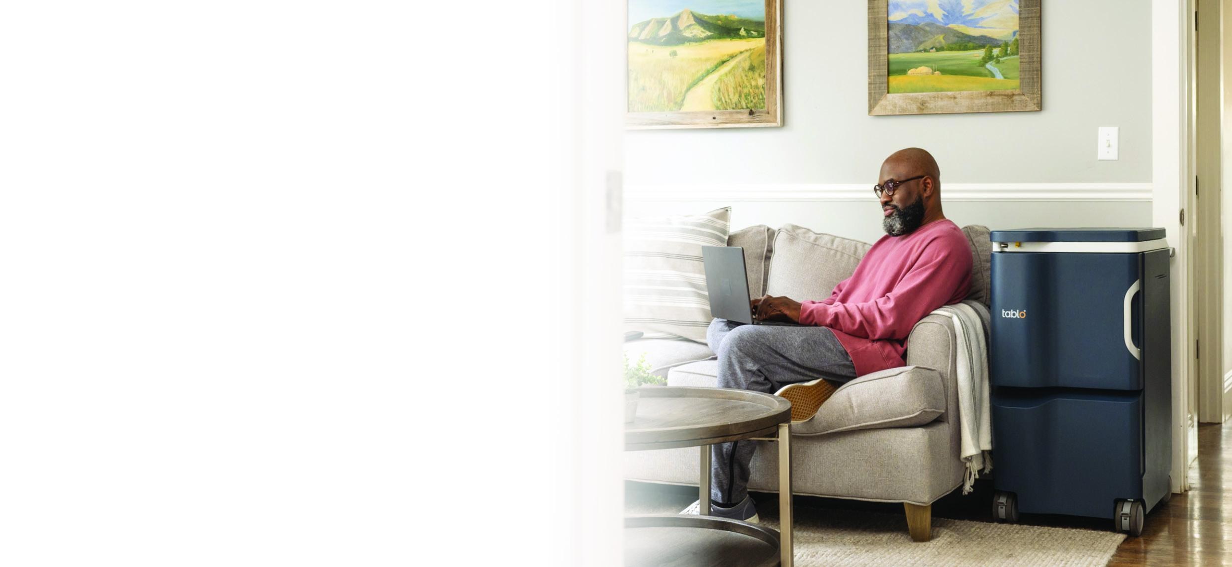 A man relaxing at home with a laptop beside a Tablo dialysis system